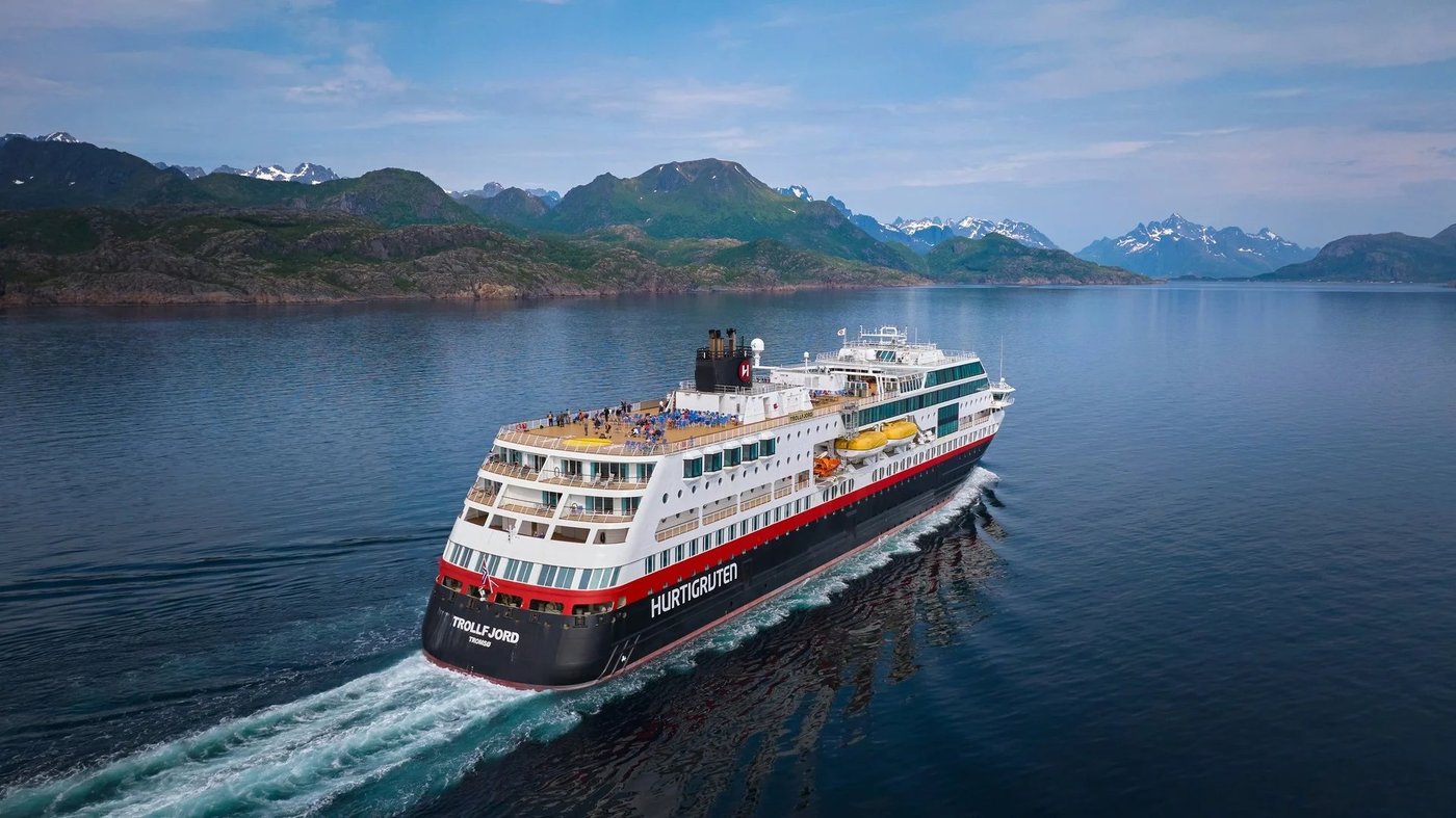 Hurtigruten coastal cruise ship sailing through Norwegian fjords with snow-capped mountains in the background.