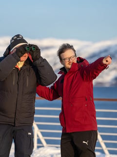 Two passengers on deck using binoculars to view the Norwegian coastal scenery during a winter cruise.