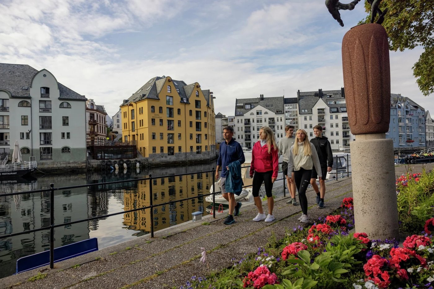 Passengers walking along the waterfront in Ålesund with colorful Art Nouveau buildings reflected in the canal.