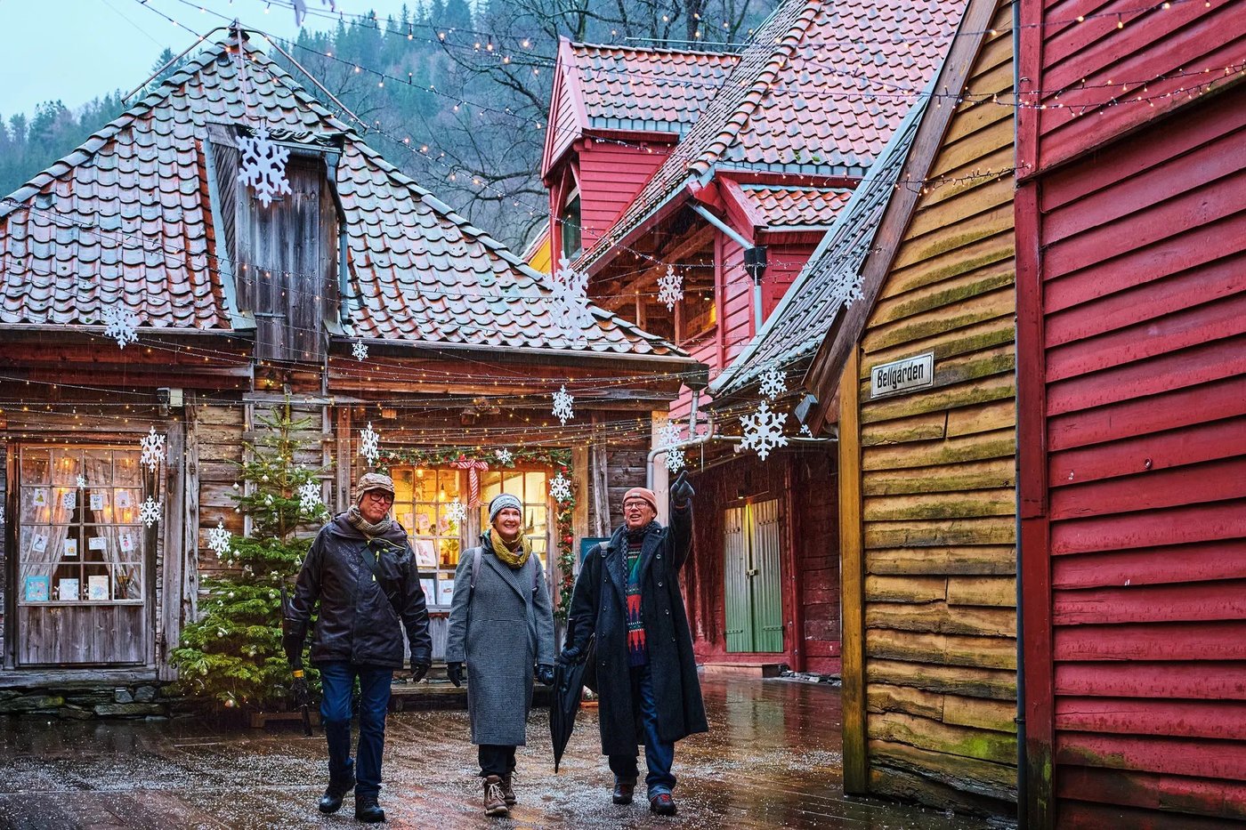 Visitors walking through the illuminated wooden buildings of Bergen's historic Bryggen wharf at dusk.