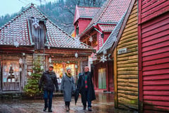 Visitors walking through the illuminated wooden buildings of Bergen's historic Bryggen wharf at dusk.