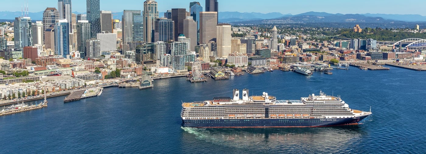 Holland America cruise ship Noordam in Seattle harbor with city skyline and mountains behind.