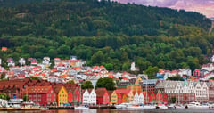 Bergen's iconic Bryggen wharf with colorful wooden buildings nestled against a forested hillside at sunset.