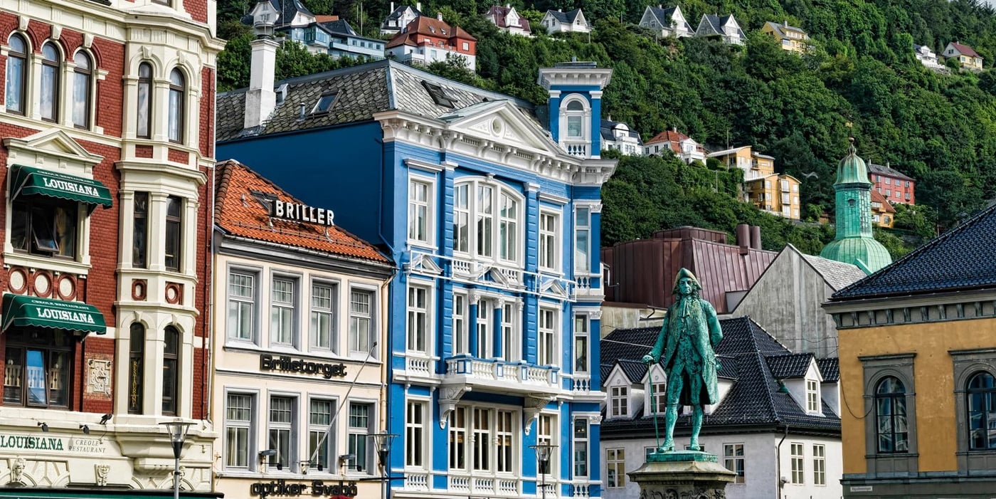 Colorful historic wooden buildings line the waterfront in Bergen, Norway, with a statue visible in the foreground.