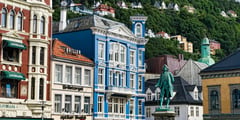 Colorful historic wooden buildings line the waterfront in Bergen, Norway, with a statue visible in the foreground.
