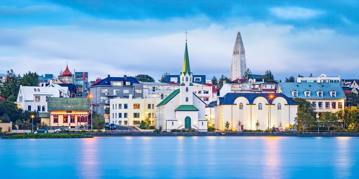 Reykjavík's waterfront skyline at dusk featuring the distinctive white church and colorful buildings reflected in calm water.