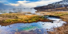 Geothermal hot spring with vivid blue water and steam rising against an Icelandic mountain landscape.