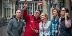 Tour guide in red jacket leading a group of passengers through a European city street.
