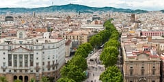 Tree-lined La Rambla boulevard stretching through Barcelona's cityscape toward distant hills.