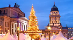 Illuminated Christmas tree and market stalls at Gendarmenmarkt in Berlin at dusk with the French Cathedral in the background.