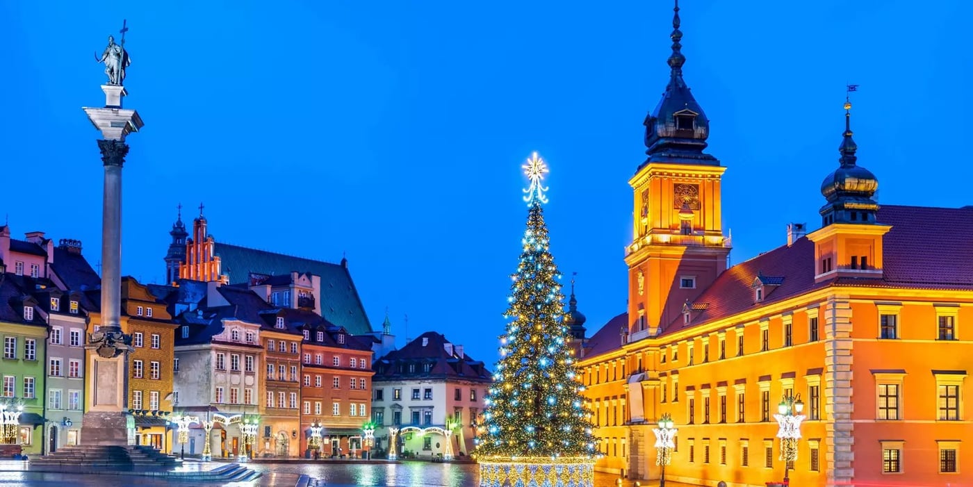 Christmas tree illuminated in Warsaw Old Town Square at night with the Royal Castle and colorful historic buildings.