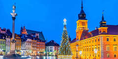 Christmas tree illuminated in Warsaw Old Town Square at night with the Royal Castle and colorful historic buildings.