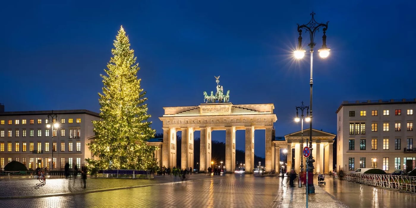 Brandenburg Gate in Berlin at night with an illuminated Christmas tree on the plaza during the festive season.