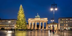 Brandenburg Gate in Berlin at night with an illuminated Christmas tree on the plaza during the festive season.