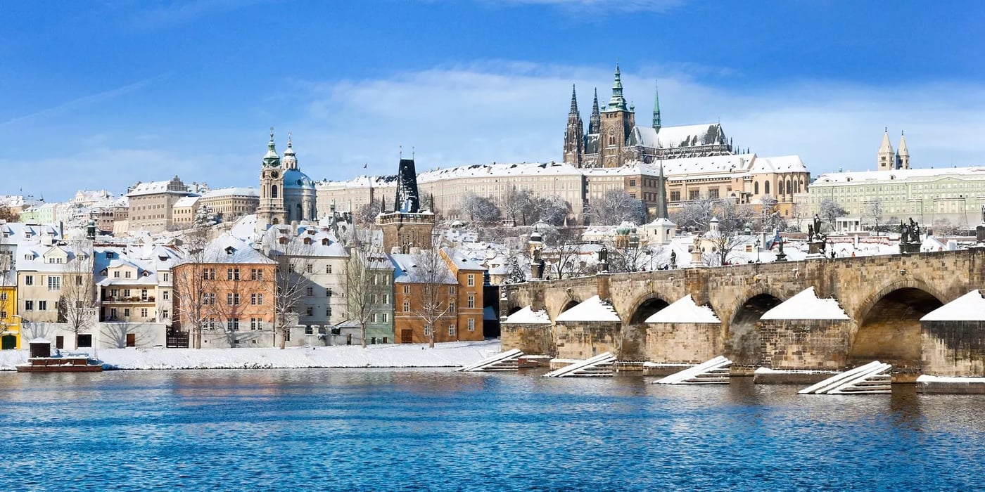 Prague Castle and St. Vitus Cathedral overlooking the Vltava River with snow-covered rooftops in winter.