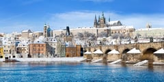 Prague Castle and St. Vitus Cathedral overlooking the Vltava River with snow-covered rooftops in winter.
