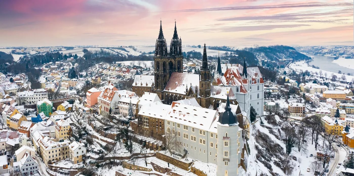 Aerial view of Meissen Cathedral and Albrechtsburg Castle covered in snow at sunset with surrounding winter landscape.