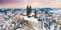 Aerial view of Meissen Cathedral and Albrechtsburg Castle covered in snow at sunset with surrounding winter landscape.