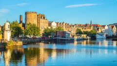 Historic waterfront buildings and boats reflected in calm harbor waters in a Scottish coastal town.