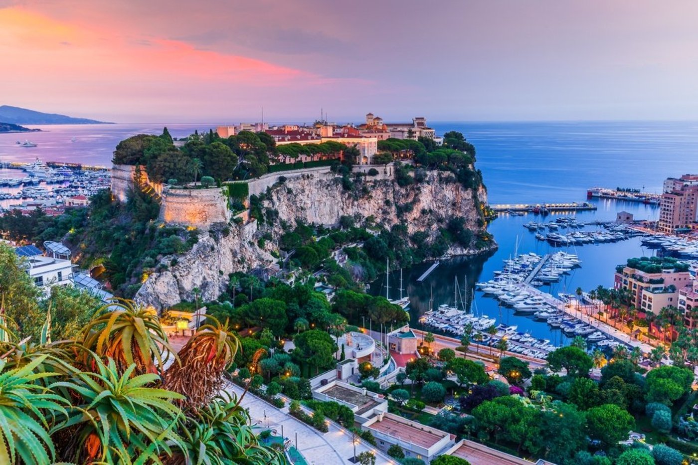 Monaco's Prince's Palace and harbor at sunset with dramatic pink and purple sky, marina, and Mediterranean coastline.