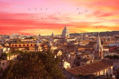 Rome cityscape at sunset with dramatic orange and pink sky, domed basilica, and birds flying overhead.