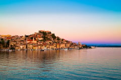 Croatian coastal town built on a hillside overlooking calm waters at sunset with pastel sky.