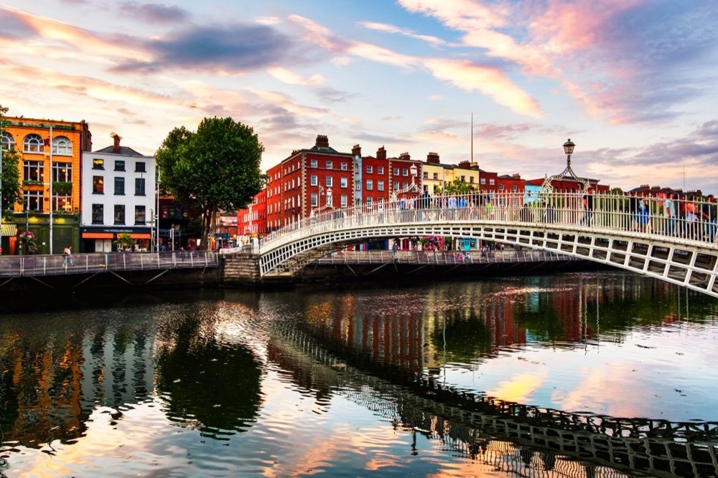 Ha'penny Bridge spanning the River Liffey in Dublin at sunset with colorful Georgian buildings lining the quay.