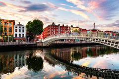 Ha'penny Bridge spanning the River Liffey in Dublin at sunset with colorful Georgian buildings lining the quay.