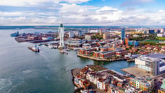 Aerial view of a harbor town with colorful buildings and a prominent white tower along the waterfront.