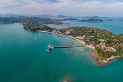 Aerial view of a tropical peninsula with a pier extending into turquoise waters in Phuket.