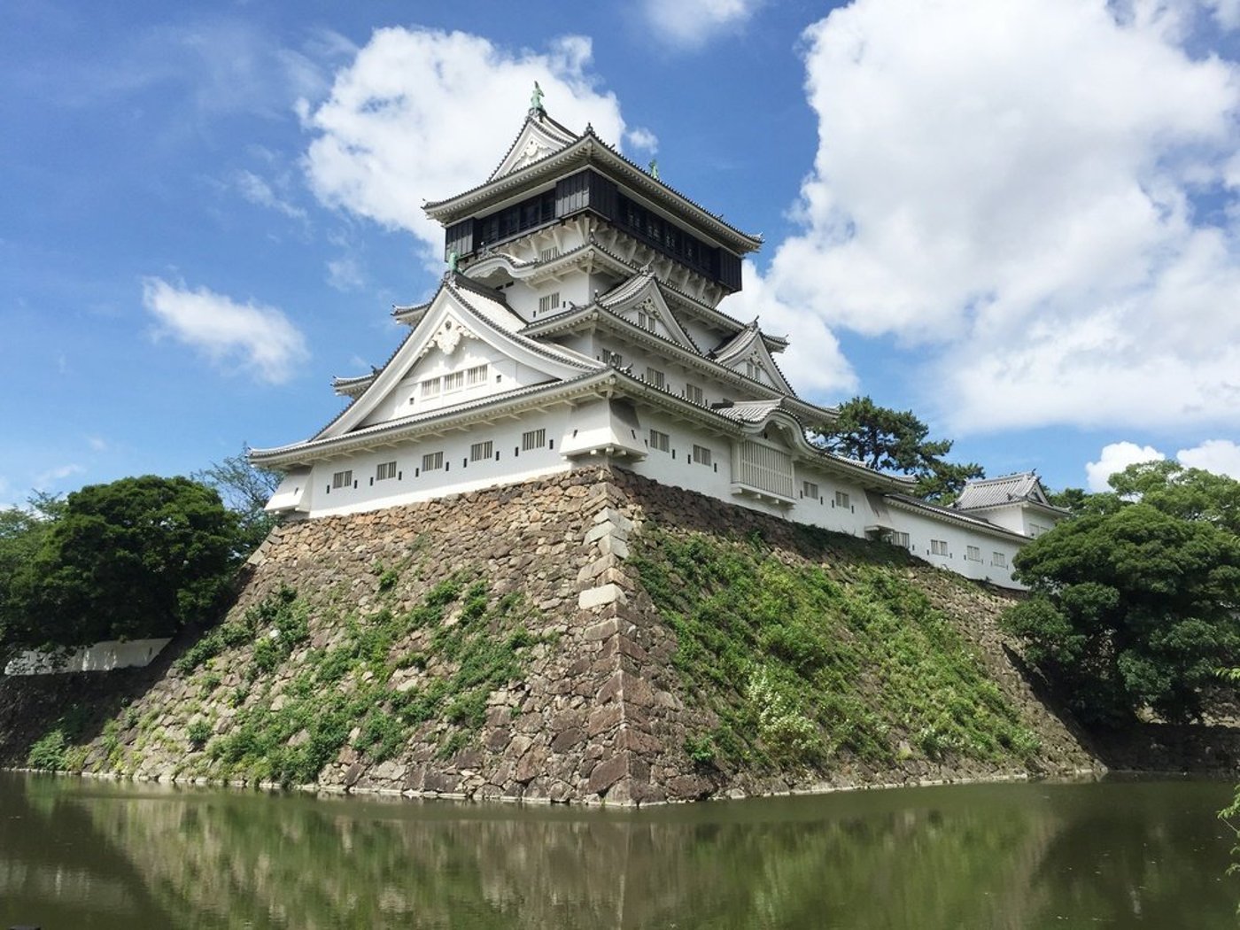Historic Japanese castle with multi-tiered architecture on stone foundation surrounded by moat and greenery.