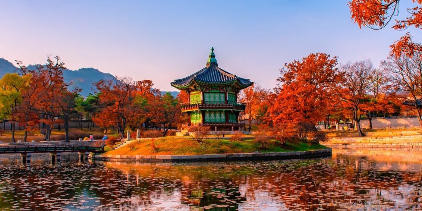 Traditional Korean pavilion reflected in a pond surrounded by autumn foliage at Gyeongbokgung Palace in Seoul.