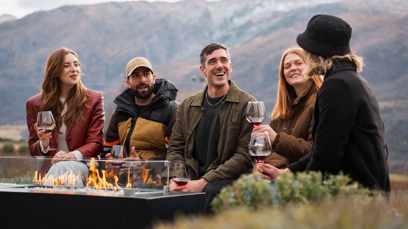 A group of travelers enjoying wine tasting at an outdoor table with mountain views in the background.