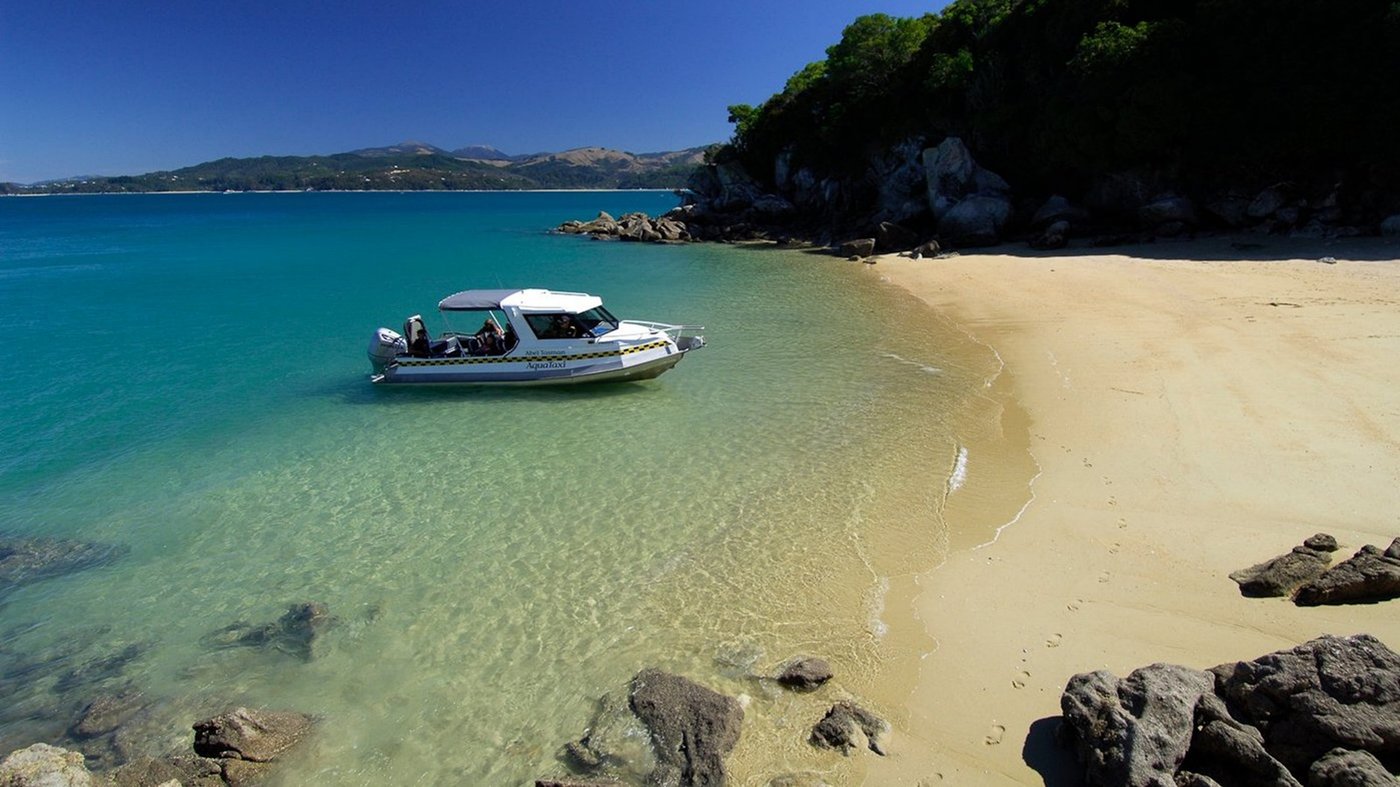 A small boat moored in crystal-clear turquoise water beside a sandy beach cove.