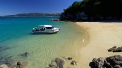 A small boat moored in crystal-clear turquoise water beside a sandy beach cove.