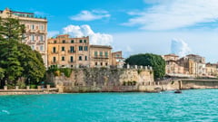 Coastal view of historic buildings and ancient fortifications along turquoise Mediterranean waters in Sicily.
