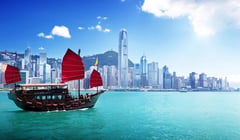 Traditional red-sailed Chinese junk boat in Victoria Harbour with Hong Kong's skyline in the background.