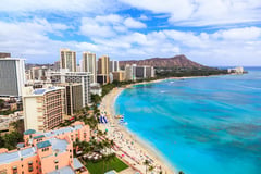 Aerial view of Waikiki Beach in Honolulu with Diamond Head crater visible in the background and turquoise ocean waters along the shoreline.