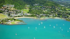 Aerial view of a turquoise bay with sailboats anchored near a coastal Queensland town surrounded by green hills.
