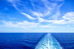 View of the ship's wake trailing through blue ocean water under a partly cloudy sky.