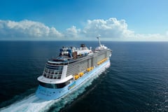 Large cruise ship sailing through open ocean waters under dramatic cloudy skies.
