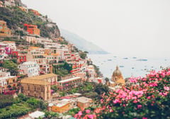 Colorful cliffside buildings of Positano cascading down to the Amalfi Coast with pink flowers in the foreground.