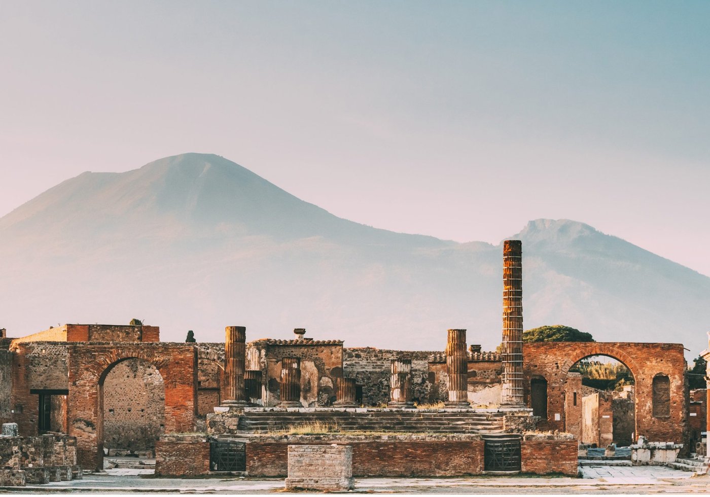 The ruins of Pompeii's forum at sunset with Mount Vesuvius in the distance.