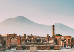 The ruins of Pompeii's forum at sunset with Mount Vesuvius in the distance.