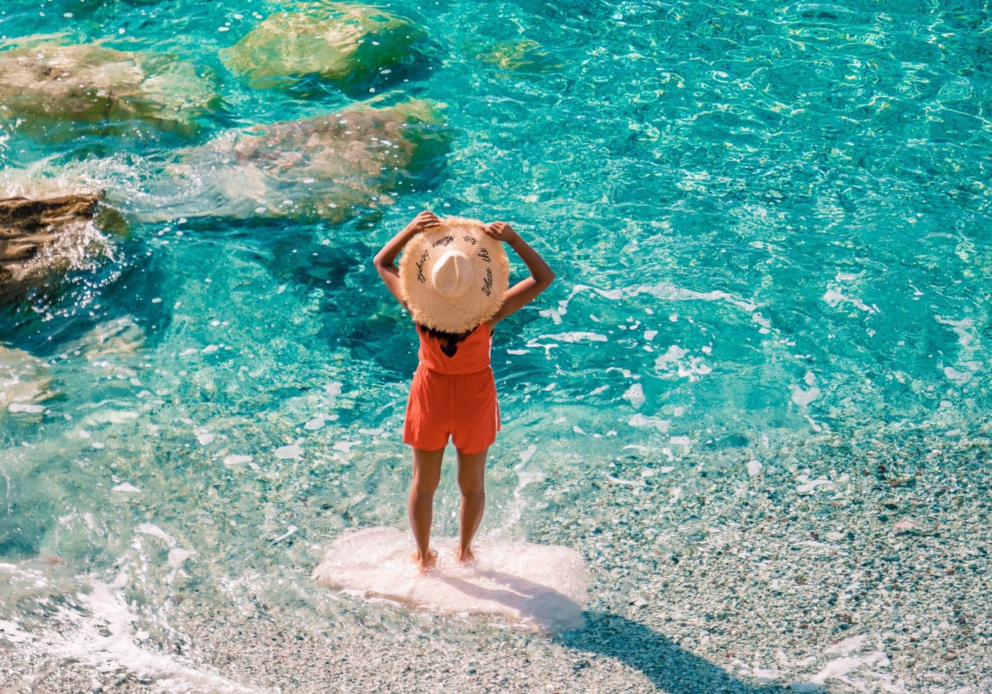 A person in an orange swimsuit standing on a rock at the edge of crystal-clear turquoise water.