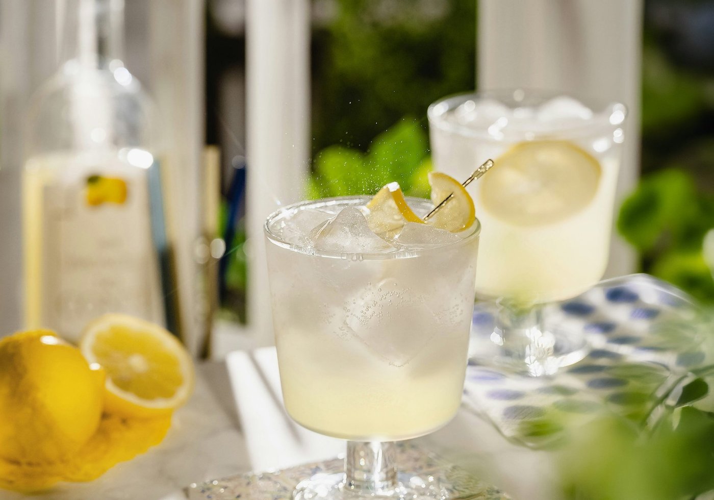 Glasses of limoncello cocktail with ice and lemon garnish on a table.